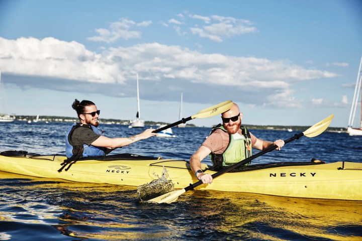 Two people in yellow kayaks smiling and paddling on a sunny day.