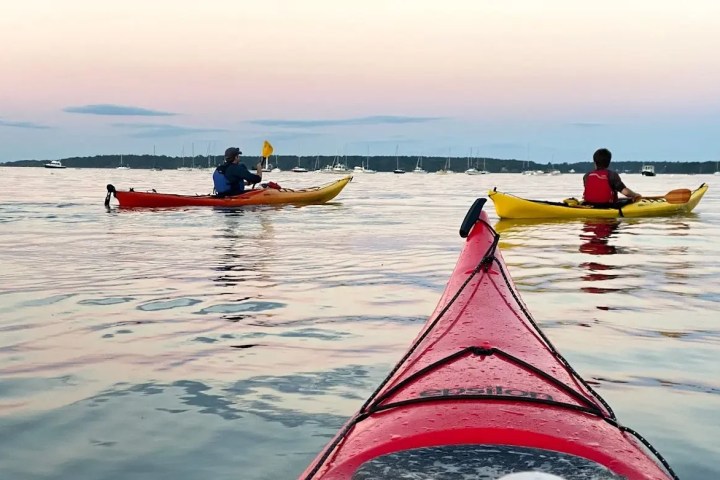 Kayakers on calm water at sunset, with a red kayak in the foreground.