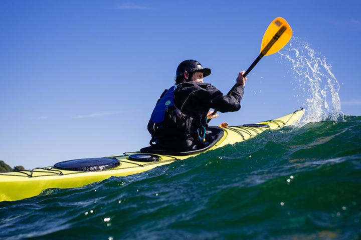 Person kayaking on blue water with yellow paddle, clear sky