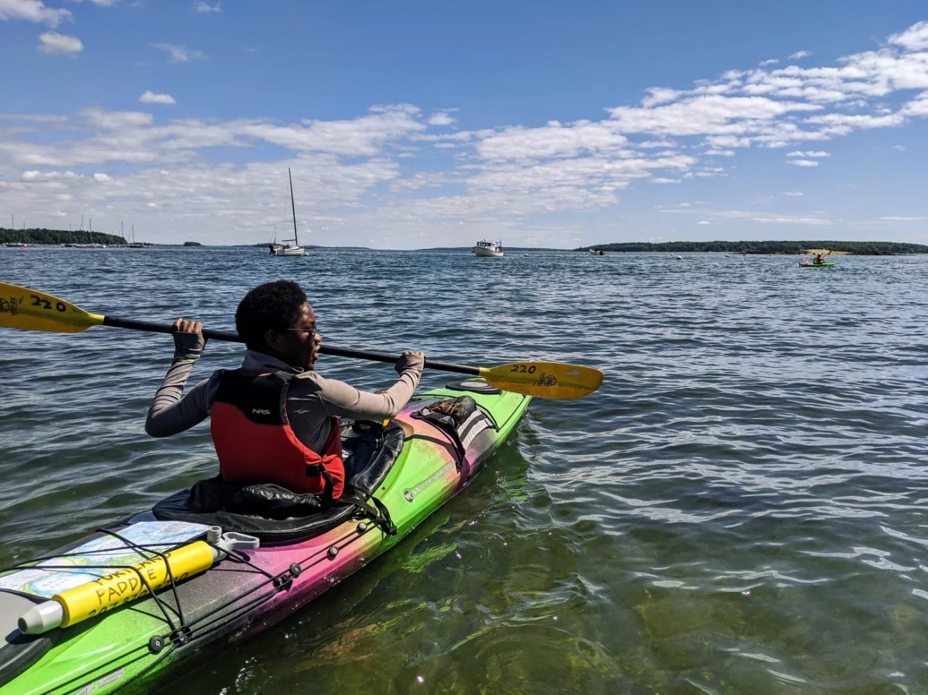 Person in a kayak paddling on a calm sea under a partly cloudy sky.